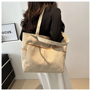 Detail of beige corduroy tote bag showing multiple pockets and brown leather piping edges