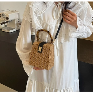 Close-up of woven straw handbag featuring bamboo handle and black leather strap