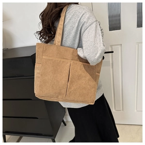 Detail view of large brown corduroy tote bag with front pockets on shoulder model