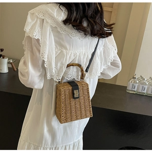 Detail of woven straw handbag featuring bamboo handle and golden metal clasp closure