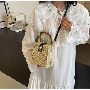 Detail of woven straw handbag featuring bamboo handle and elegant metal turn-lock closure