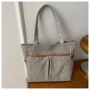 Details der hellgrauen Cord-Tasche mit großen Taschen und brauner Verzierung am Rand
