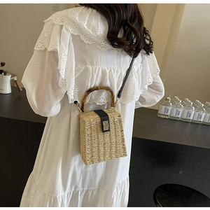 Detail of woven straw handbag featuring bamboo handle and leather clasp closure