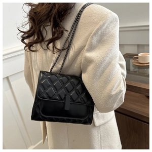 Close-up of black quilted shoulder bag with metal chain strap on a model for urban style