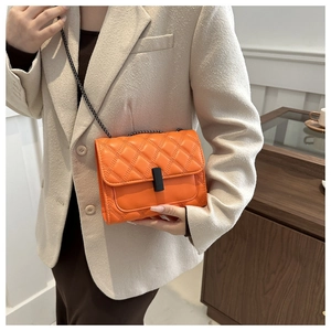 Close-up of orange quilted crossbody bag with black matte metal lock and chain strap