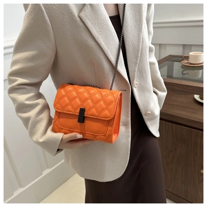 Detail of orange quilted crossbody bag with matte black lock and chain strap on model