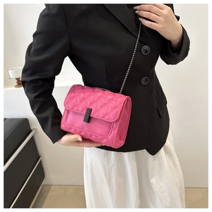 Pink quilted crossbody bag with black metal chain shown on model in minimal indoor setting