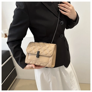 Beige quilted chain crossbody bag with black metal clasp worn with a modern outfit