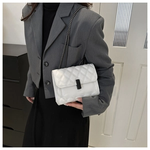 Close-up of white quilted chain bag with black clasp worn as a crossbody shoulder bag