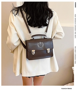 Detail of dark brown matte leather bag featuring an academic shield badge on white blazer