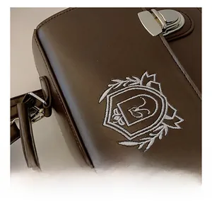 Detail of vintage JK uniform bag featuring brown leather texture and white embroidery