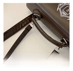 Close-up of dark brown leather handbag featuring a comfortable handle and embroidered badge