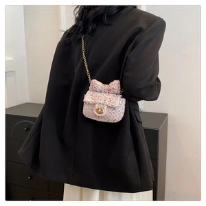 Detail of pink tweed crossbody bag with bow accent and golden chain on model