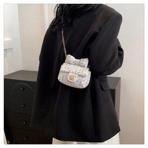 Detail of tweed crossbody mini bag with bow accent and gold chain on black blazer