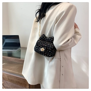 Detailed shot of black tweed crossbody bag featuring golden lock and bow accent