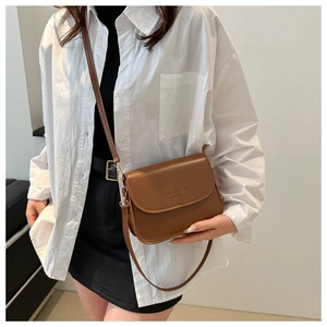 Détail du sac bandoulière en cuir marron caramel avec texte embossé et rabat élégant