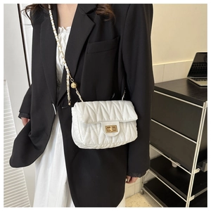 Detail of white matelassé leather saddle bag with gold chain strap and metal ball decor