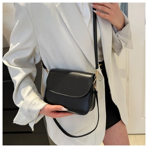Détail du sac à bandoulière noir avec finitions dorées porté sur un blazer blanc