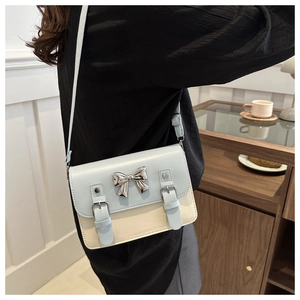 Detailed view of bicolor crossbody bag with silver bow buckle on the cream leather body