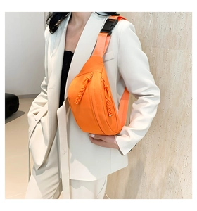 Dettaglio della borsa a tracolla in nylon arancione con doppia zip su un blazer bianco