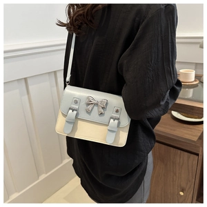 Detail of light blue and beige crossbody bag with silver bow accent on minimalist background