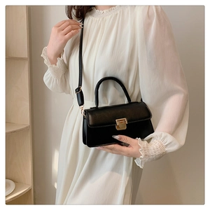 Detail einer schwarzen Handtasche mit goldenem Metallschloss und elegantem Tragegriff