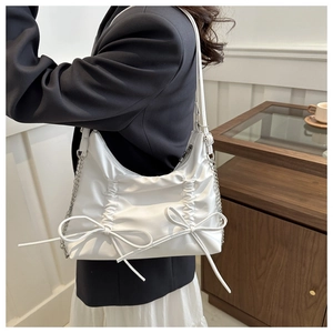 Detailed side view of white pleated underarm bag with decorative bows and silver chain straps