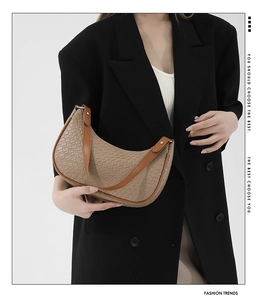 Detail of a khaki woven hobo bag worn with a black blazer in a minimalist fashion shot