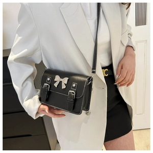 Detail of black crossbody bag featuring a silver metal bow and white contrast stitching
