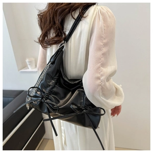 Detail of black pleated shoulder bag with bow decor and silver chain on a white dress