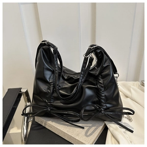 Detail of black pleated tote bag featuring decorative leather bows and metal chain strap