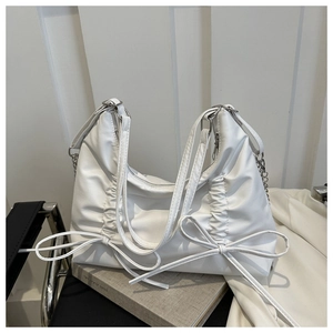 Close-up of white pleated shoulder bag with decorative bow ties and metal chain strap