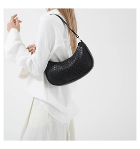 Detail of black crescent shoulder bag with embossed crocodile pattern on white outfit