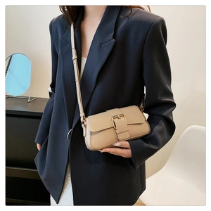 Detail of stylish beige crossbody bag with large gold buckle and adjustable strap on a model
