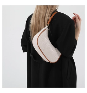 Minimalist cream crocodile pattern crescent bag worn on shoulder by model in black suit