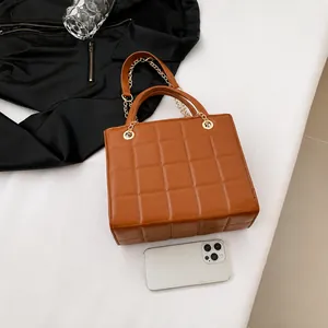 Brown quilted handbag with chain strap shown with smartphone for size reference