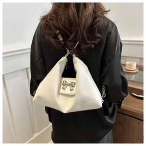 Close-up of white leather tote bag with silver metal bow and chain strap on shoulder