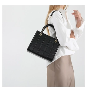 Detail of black quilted tote bag with golden chain strap and luxury leather texture