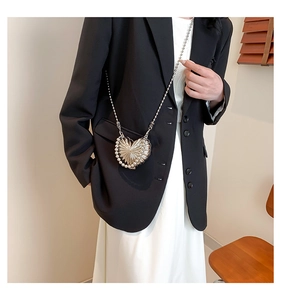 Détail du sac coeur argenté avec perles et chaîne porté sur un tailleur noir chic