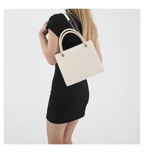 Quilted cream crossbody bag with gold chain strap shown on a black dress background