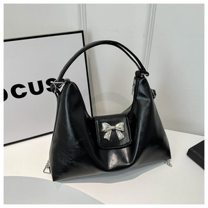 Detail of silver bow accent on black leather tote bag with glossy finish and metal chain