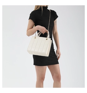 Close-up of quilted cream tote bag with gold chain strap on model in black dress