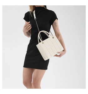 Detailed view of white quilted square bag with gold chain strap on black dress