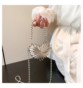 Detailed view of a silver heart-shaped metal bag with pleated texture and pearl handle