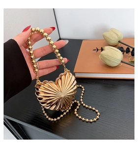 Macro shot of gold heart-shaped metallic mini bag featuring radial textures and bead chain