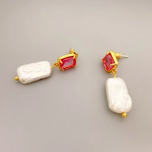 Detailed macro view of baroque pearl earrings with rectangle red gemstones and gold settings