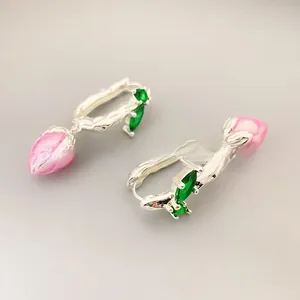 Macro shot of silver-plated hoop earrings featuring pink enamel tulip buds and green gems