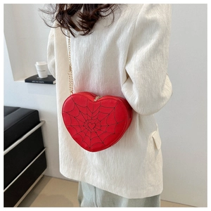 Detail of red heart bag with spider web pattern and gold chain strap worn by a model