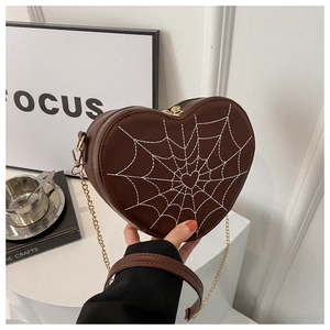 Macro detail of heart-shaped crossbody bag with white spiderweb embroidery and gold chain