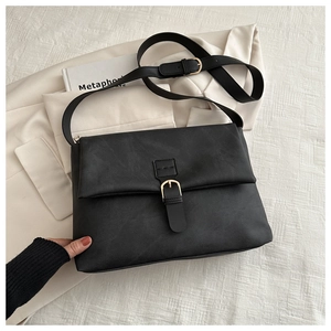 Détail d'un sac cabas noir mat avec boucle dorée sur un fond de costume beige